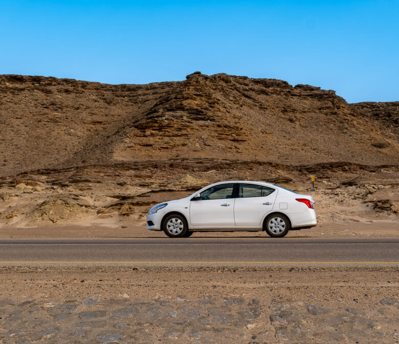 Mietwagen auf Straße im Oman und im Hintergrund Berge und blauer Himmel