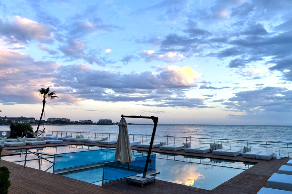 Ein Pool mit Kissen, einer Palme, und im Hintergrund das Meer