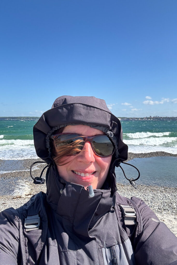 Eine Frau mit Kapuze und Sonnenbrille vor dem Meer
