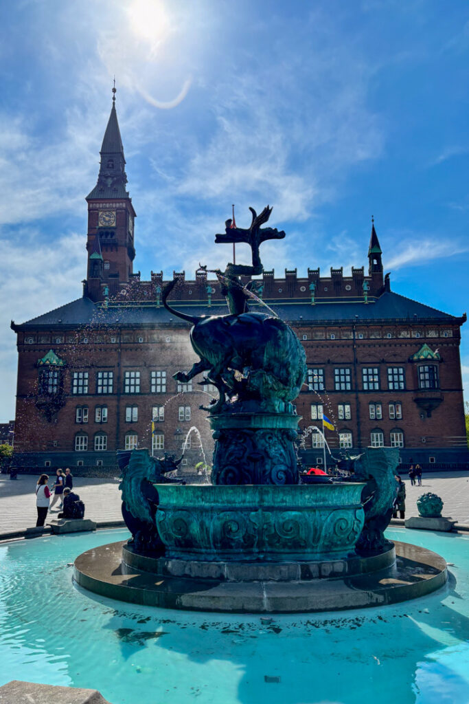 Ein Brunnen im Vordergrund und dahinter ein großes Gebäude mit Turm