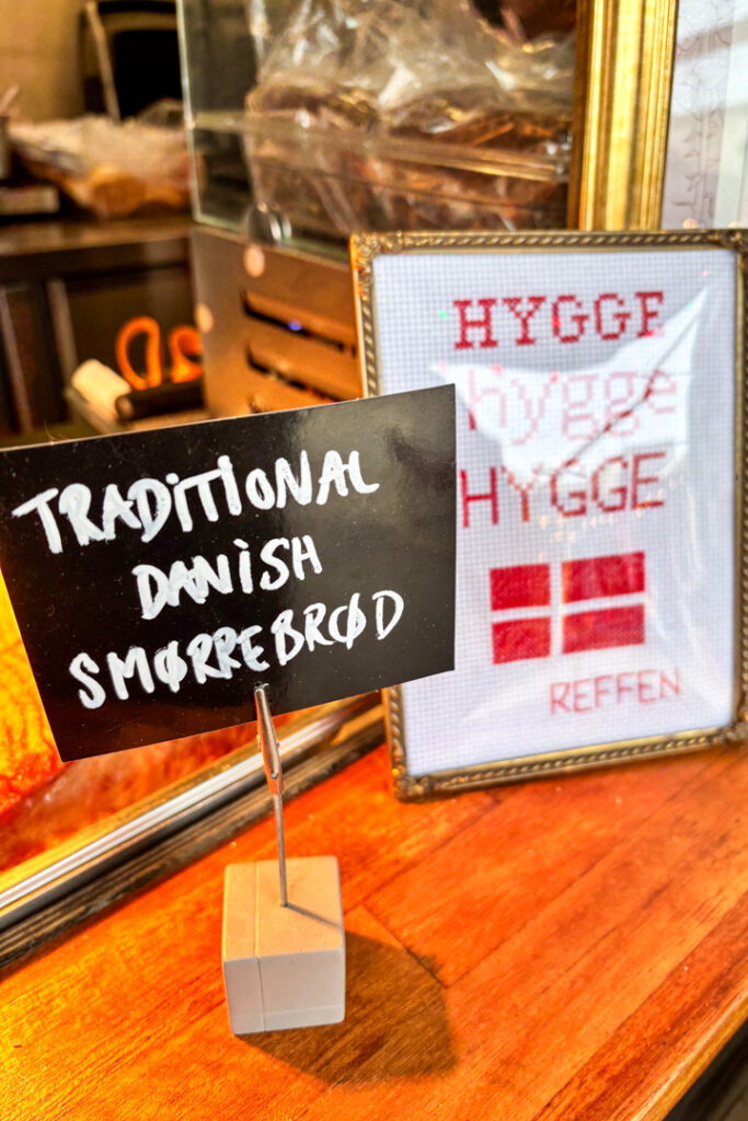 Ein Schild auf einem Ständer neben einem "Hygge"-Schild