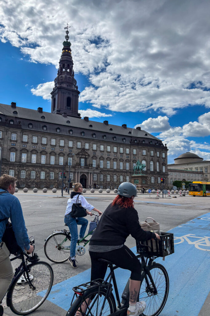 Drei Fahrradfahrer und dahinter ein Gebäude mit Turm
