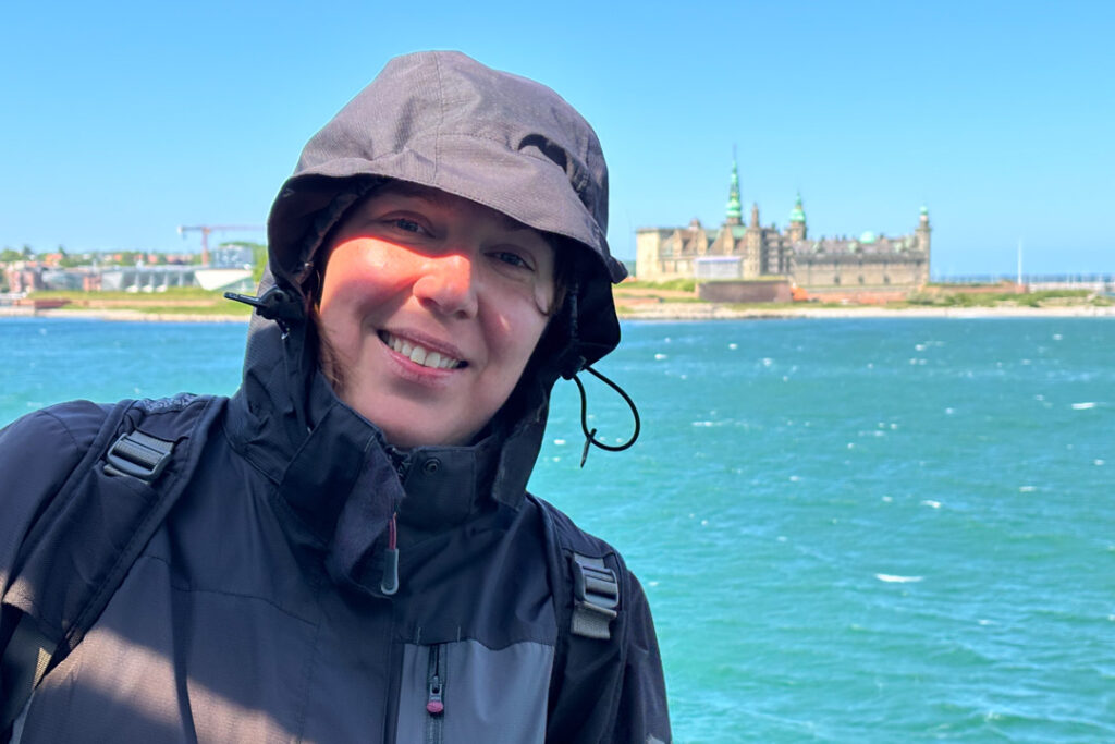 Eine Frau steht vor blauem Wasser und einem Gebäude