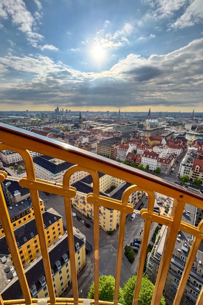 Ein gelbes Geländer im Vordergrund und dahinter viele Gebäude und die Sonne