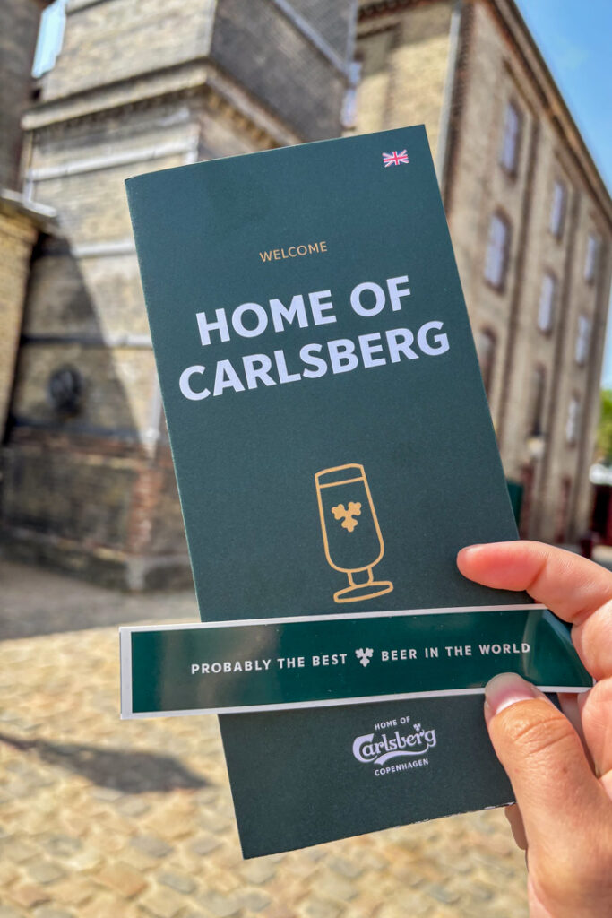 Eine Hand, die ein grünes Prospekt mit der Aufschrift "Home of Carlsberg" in der Hand hält