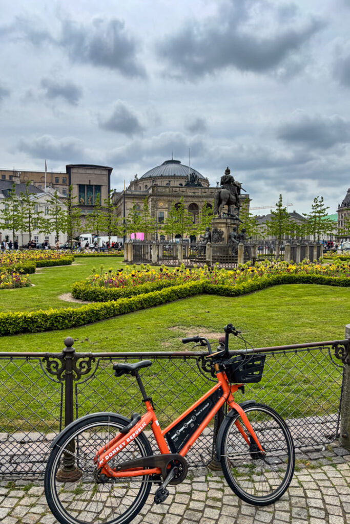 Ein rotes Fahrrad, welches am Geländer lehnt, dahinter eine Grünfläche und ein Gebäude mit Kuppel