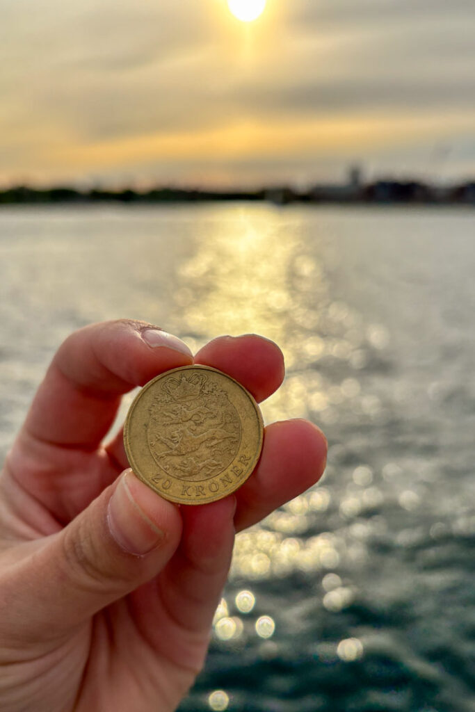 Eine Hand, die eine Münze hält vor einem Fluss mit untergehender Sonne