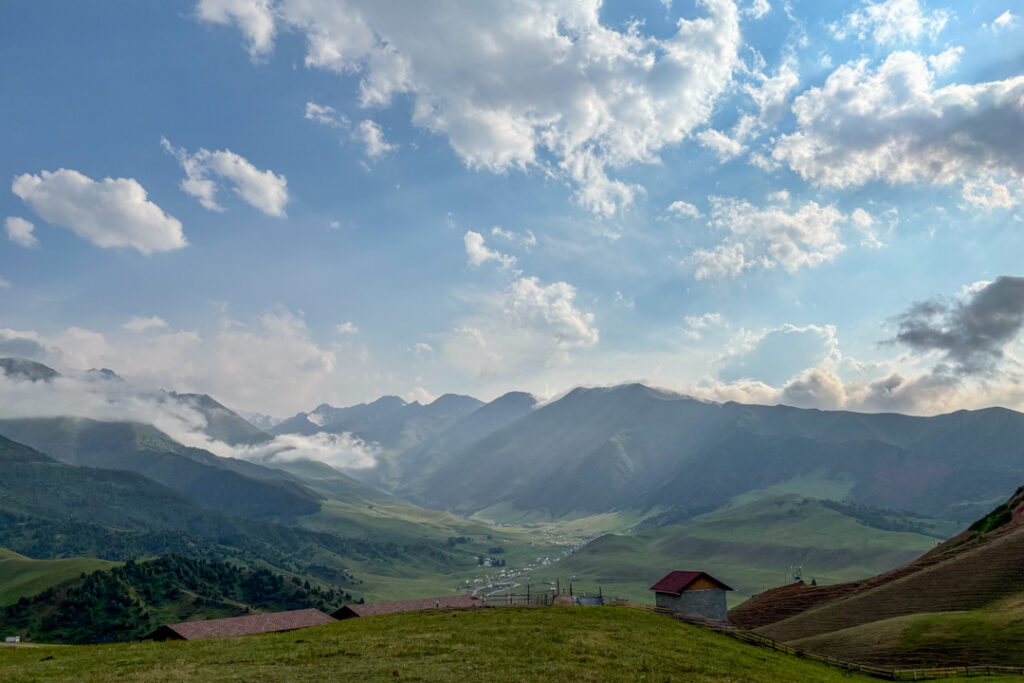Ein weites grünes Tal mit Bergen, Wolken und Jurten 