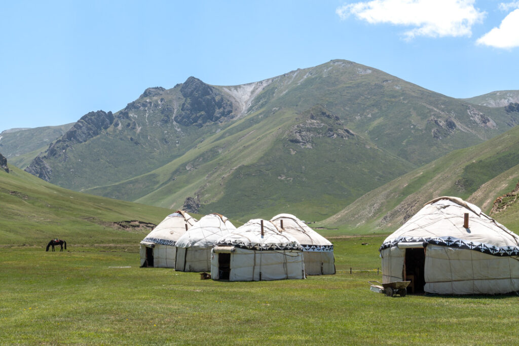Jurten, ein Pferd und Berge im Hintergrund