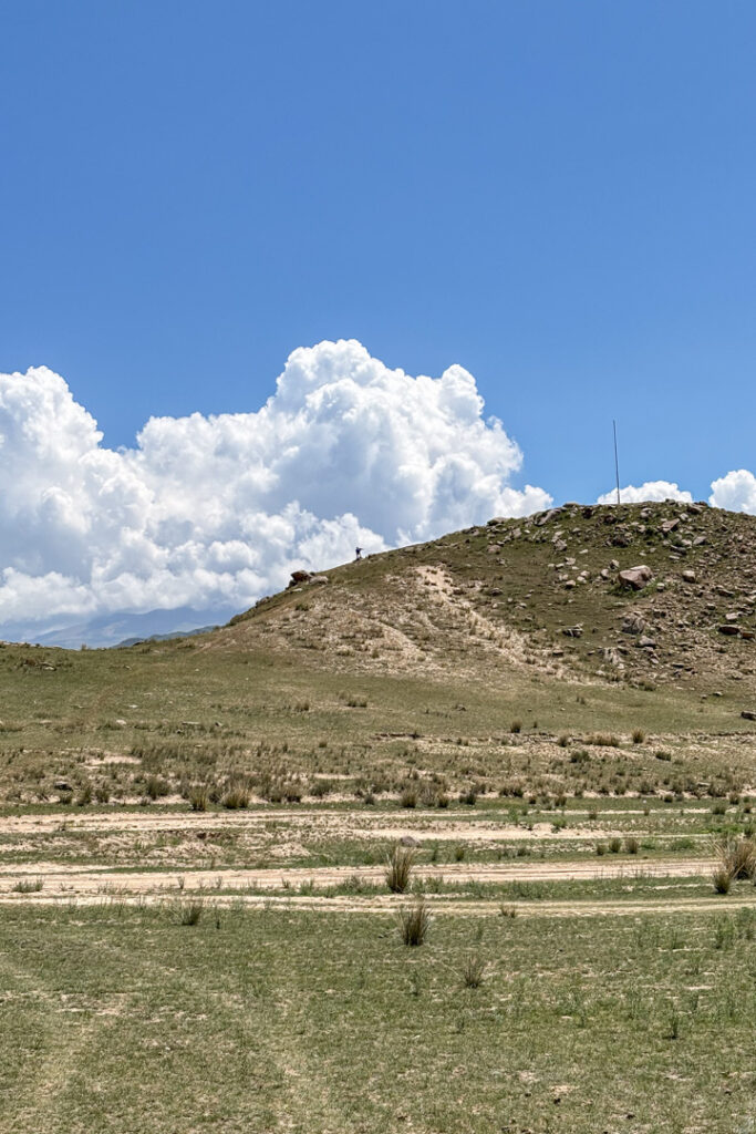 Ein grüner Hügel mit Wolken und einem Mensch weit weg