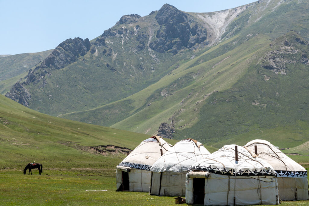 Drei weiße Jurten und ein Pferd in einer Berglandschaft