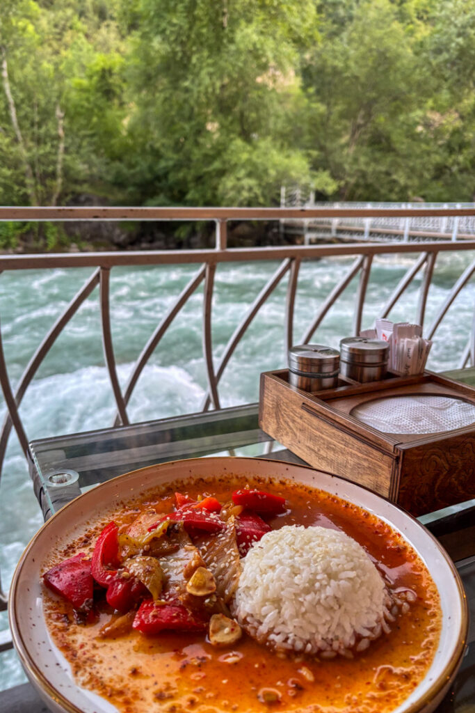 Ein Teller mit Gemüse und Reis und dahinter ein rauschender Fluss 
