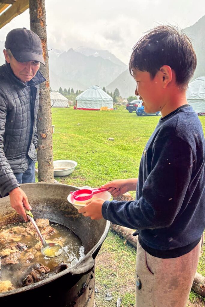Ein Junge und ein Mann, die an eine großen Kessel mit eine toten Tier stehen, was darin gekocht wird