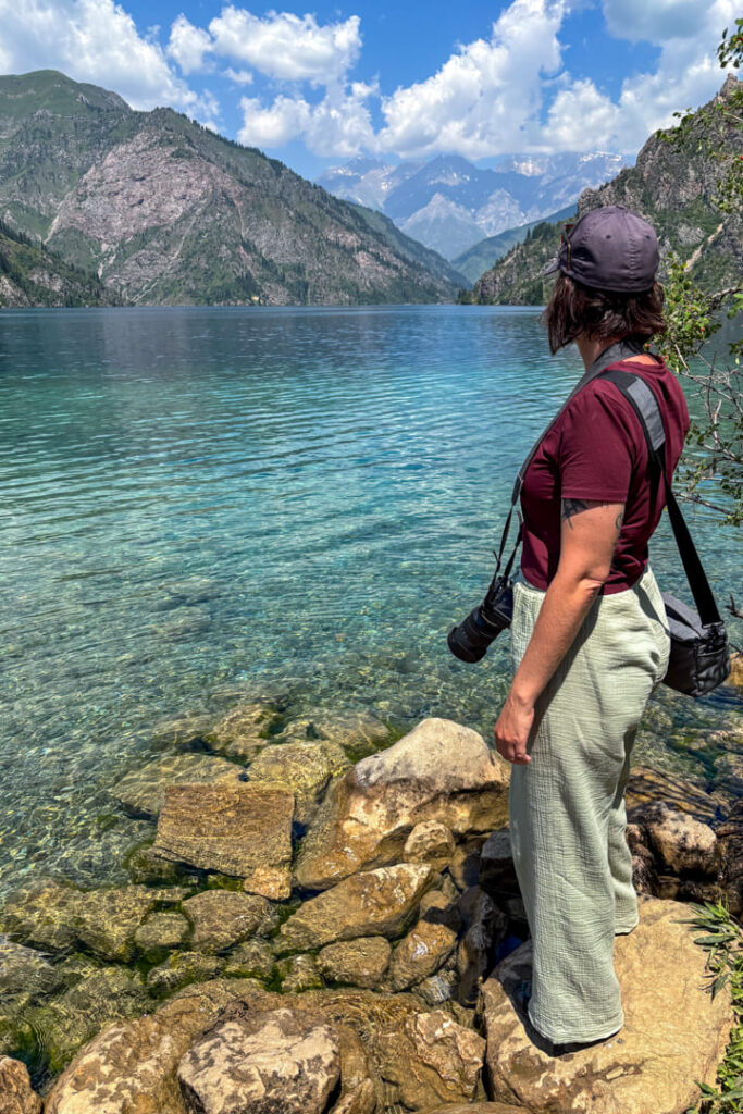 Eine Frau steht an einem blauen See und blickt in die Ferne 