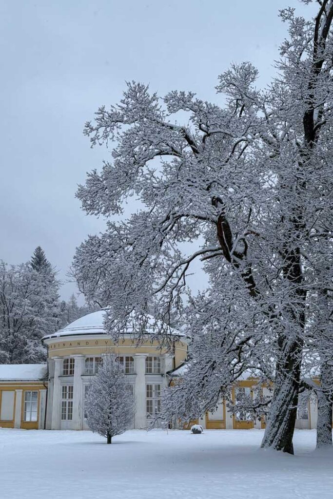 Eine gelbe, überdachte Kolonnade mit Kuppel im Schnee, umgeben von schneebedeckten Bäumen