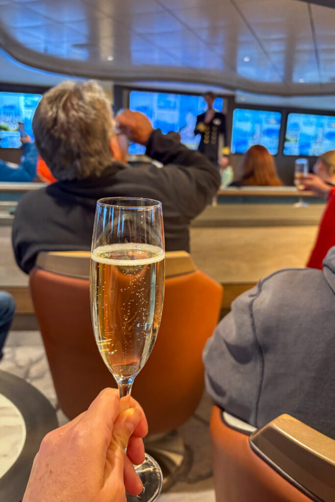 Eine Hand hält ein Glas Sekt nach oben, im Hintergrund eine Lounge