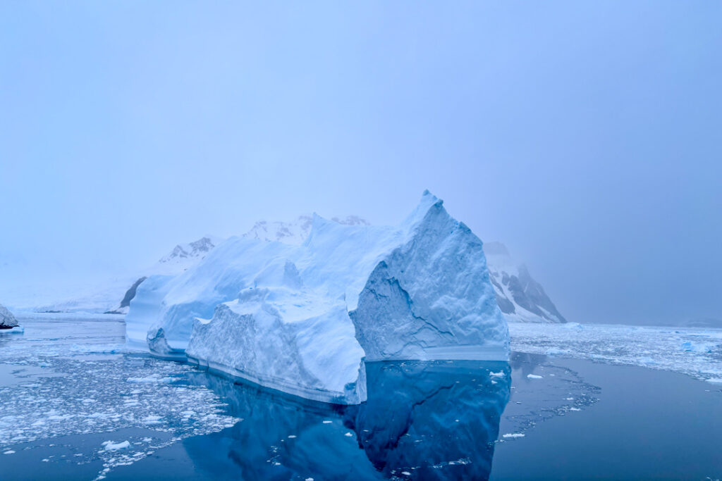 Ein großer blauer Eisberg mit einer Spitze, der sich im spiegelglatten Wasser spiegelt