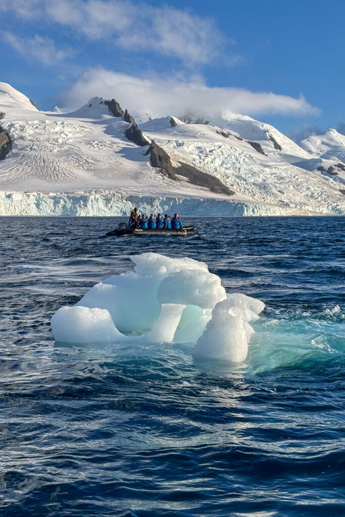 Ein schwarzes Zodiac-Boot fährt auf dem blauen Meer, im Vordergrund ein kleiner Eisberg