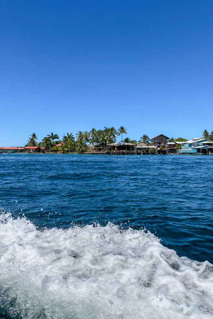 Blick auf eine Insel von einem Boot aus, im Vordergrund schäumt das Wasser auf
