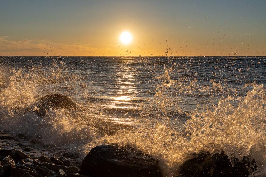 Sonnenuntergang und brechende Wellen mit Steinen im Vordergrund