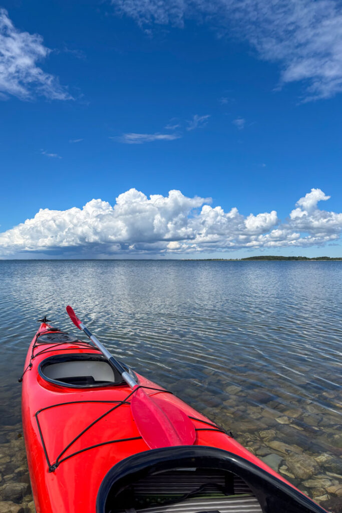 Ein rotes Kajak liegt am Ufer und im Hintergrund bäumen sich weiße Wolken auf