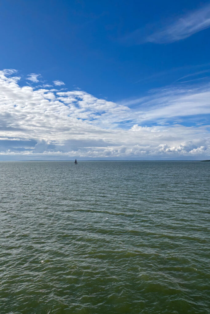 Blaues Meer und Himmel vom Wasser aus fotografiert, in weiter Ferne ein Segelboot