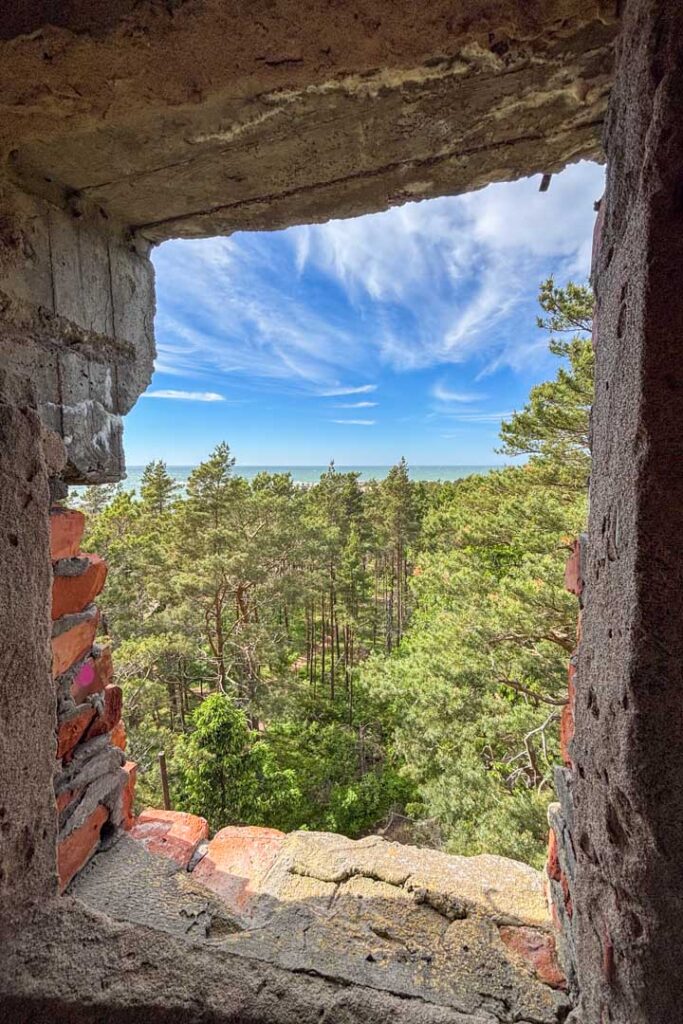 Ausblick durch einen eckigen Rahmen aus Stein, man sieht viele grüne Bäume und Meer