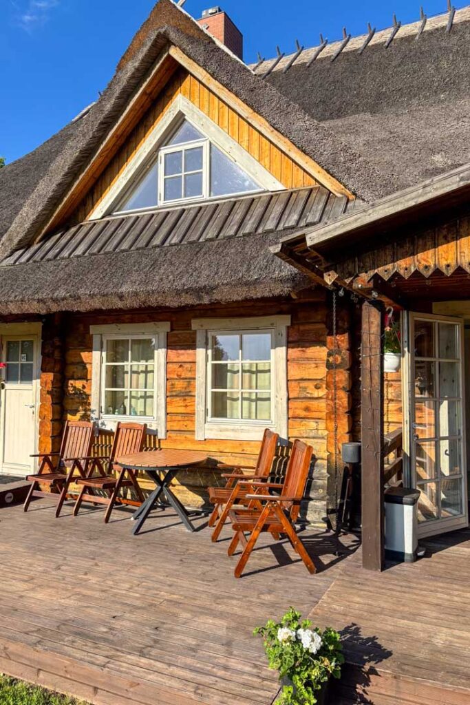 Eine gemütliche Holzterrasse vor einem Blockhaus mit Reetdach, ausgestattet mit Holzsitzgruppen im warmen Sonnenlicht