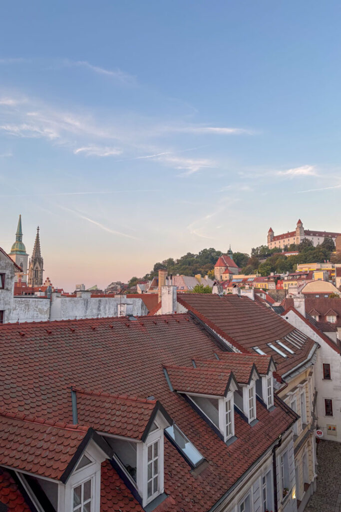 Panoramablick über die roten Ziegeldächer von Bratislava im warmen Abendlicht, mit den Türmen des Martinsdoms links und der Burg Bratislava rechts auf dem Hügel